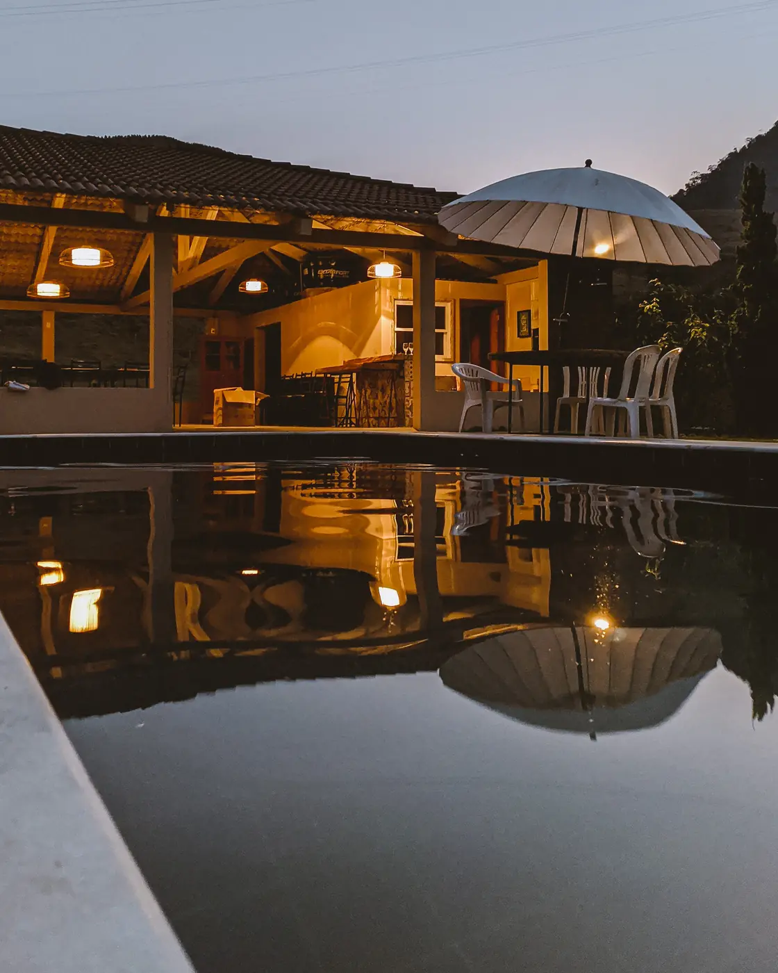 Salão de festas iluminado ao anoitecer, refletido na piscina
