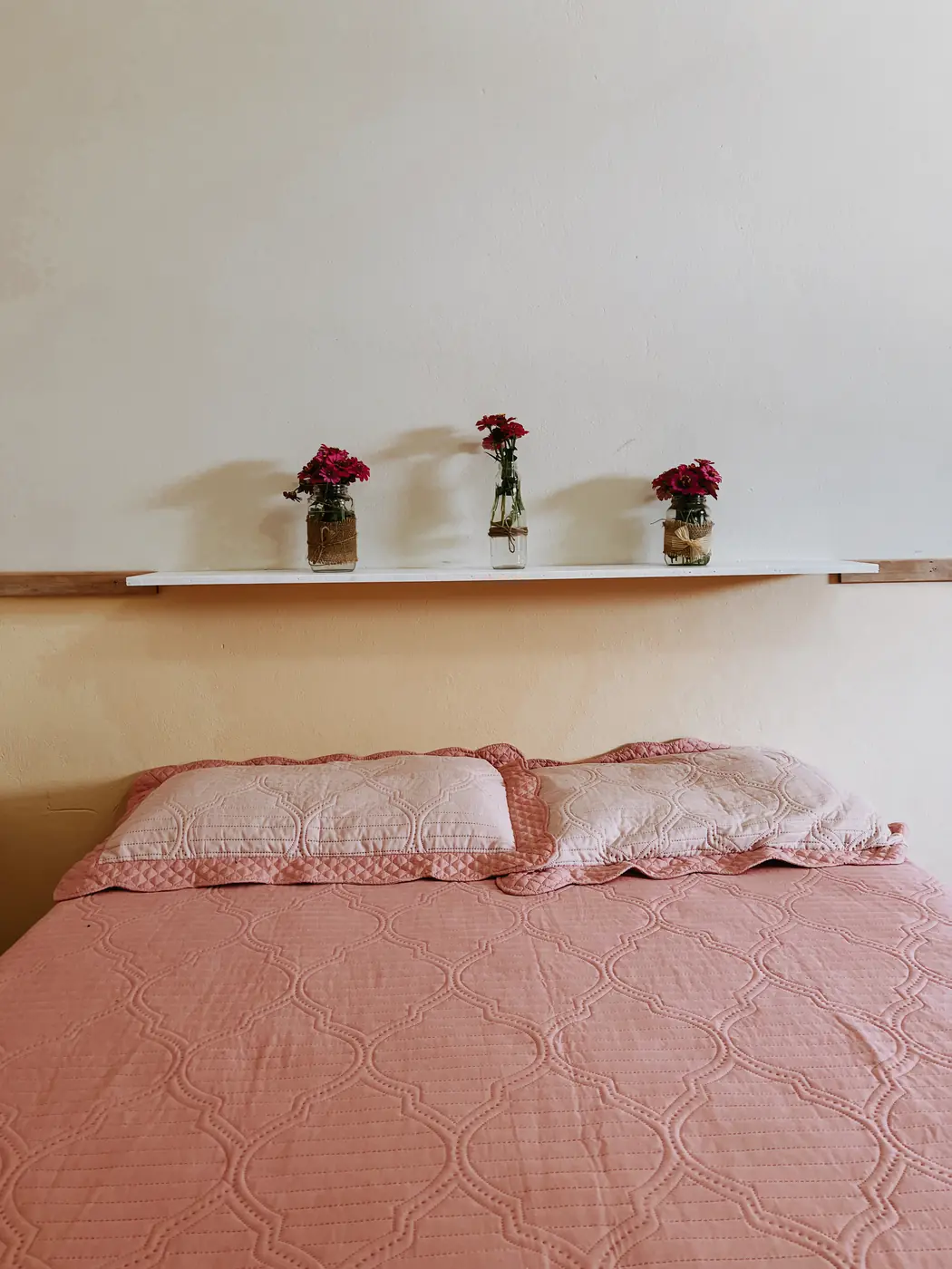 Cama de casal com colcha rosa e flores na prateleira